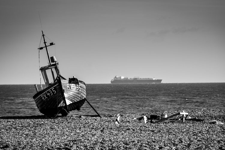 Boat on the shoreline with a tanker in the distance juxtaposed