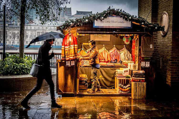 Man walking past a lit up pop up shop in the rain